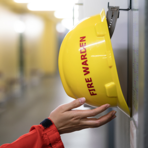 Fire Warden reaches for fire safety hat during a Fire Warden Training course held in Australia and taught by Fire Safe Australia and New Zealand. This image features a yellow fire warden cap, with red writting.
